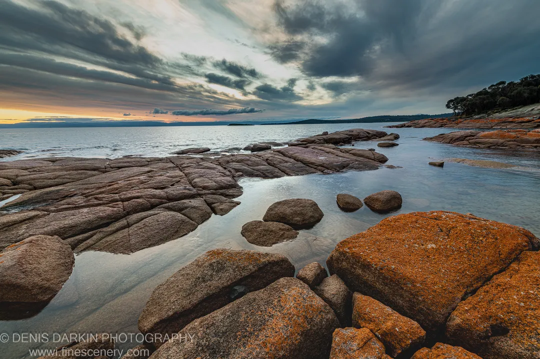 Pink granite shelves and pools at Coles Bay, with storm clouds on one side and a soft sunset glow on the other.