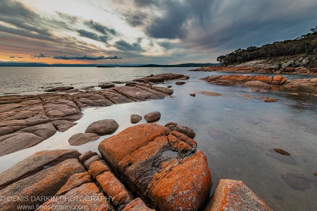 Moss-covered granite boulders reflect in still tidal pools at Coles Bay, while cloud formations above transition from warm sunset hues to cool grey, April 2022.