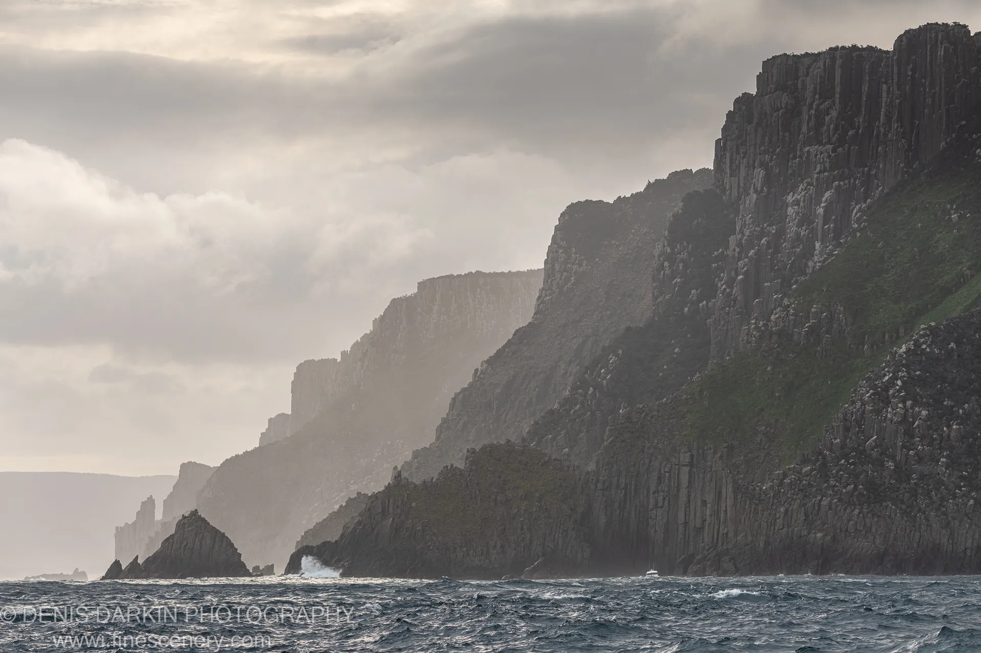 Tall columnar basalt cliffs recede into misty haze above a rough sea at Cape Pillar, Tasman Peninsula, April 2022.