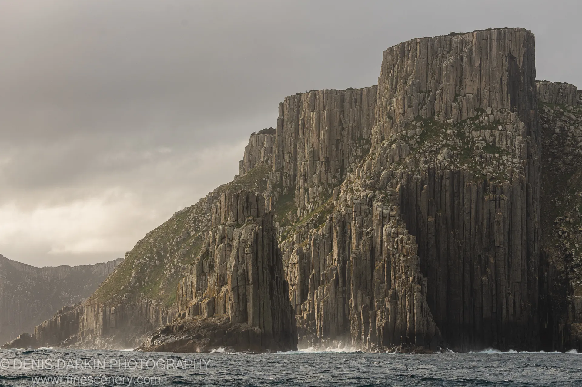 Light-coloured vegetation on ledges of dark columnar basalt at Cape Pillar, Tasman Peninsula, under overcast afternoon light, April 2022.