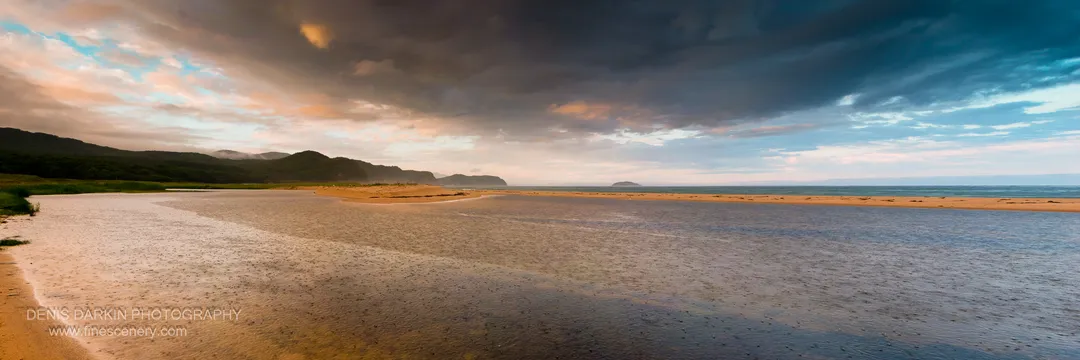 Wet tidal flats at Tachingouza Bay under heavy storm clouds at dusk, with patches of warm light reflected in the wet sand, July 2010.