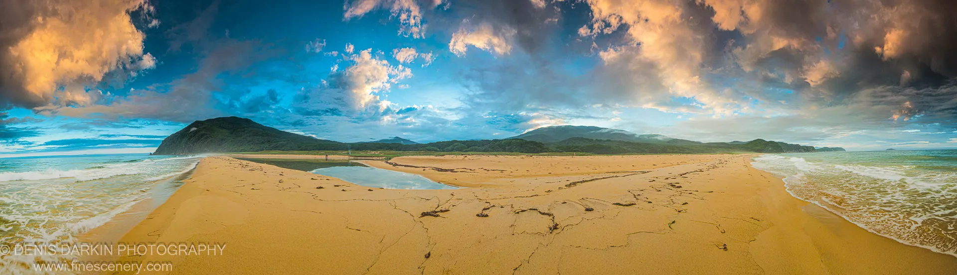 Warm light on wet sand and tidal pools at Tachingouza Bay at sunset, with white surf in the middle distance and headlands behind, July 2010.