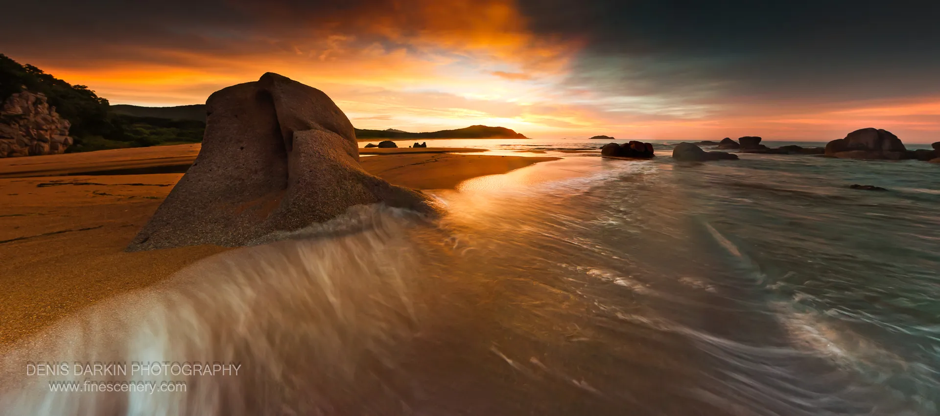 A large granite boulder on wet sand at Tachingouza Bay, with long-exposure surf and an orange dawn sky reflected in the sand, July 2010.