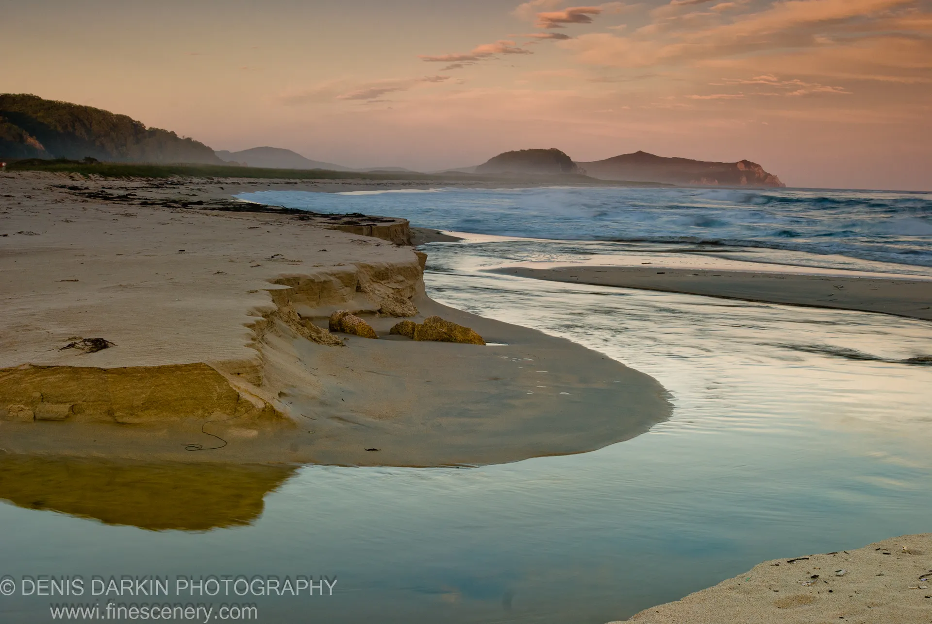 Warm-lit sand cliffs rise above a shallow inlet pool, with misty headlands visible in the distance, Lazovsky Reserve.