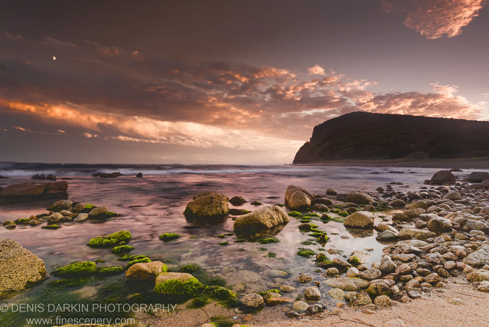 Moss-covered boulders and tidal pools on the rocky shore at Petrova Island, Lazovsky Reserve, with long-exposure water and a silhouetted headland at dusk.