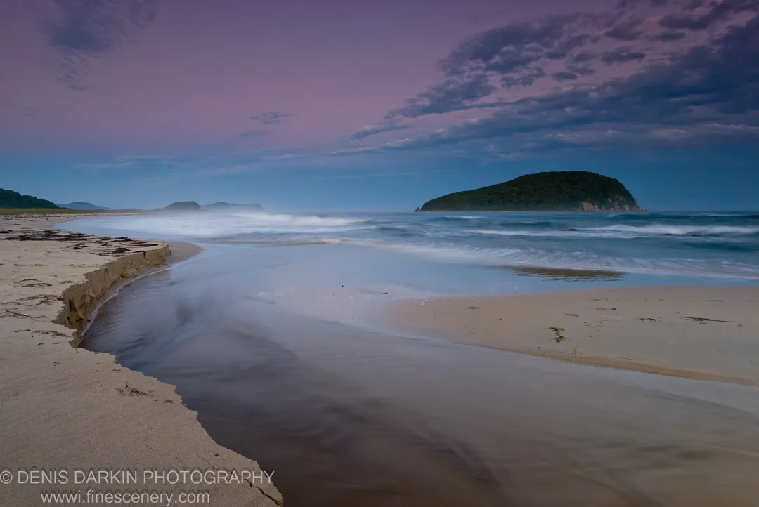 Wet sand and a shallow inlet extend toward a dark forested island on the right under a violet dusk sky at Petrova Island, Lazovsky Reserve.