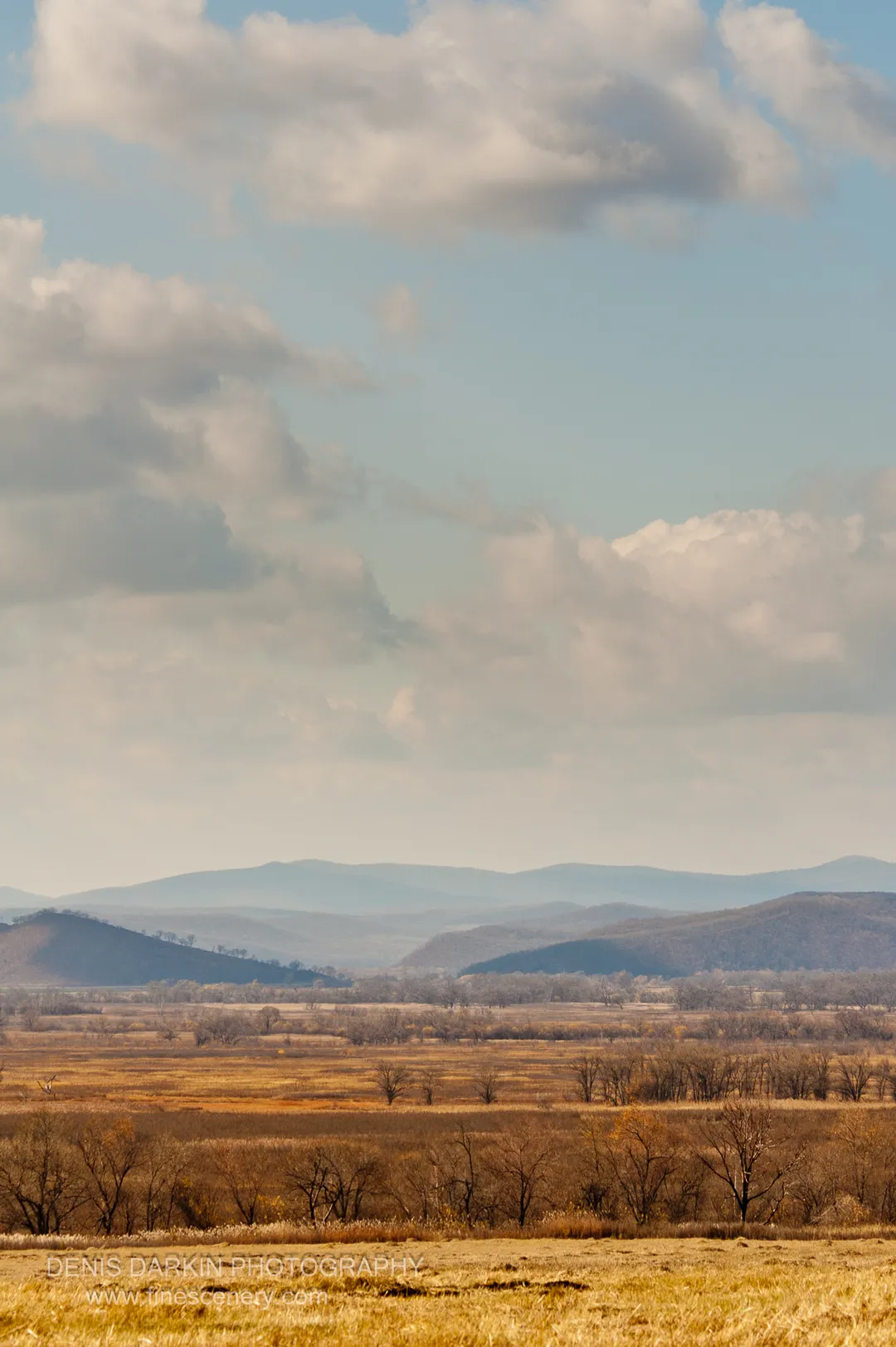 A vertical composition of rolling hills fading into atmospheric haze under a broad sky of white clouds, Chuguyevsky District.