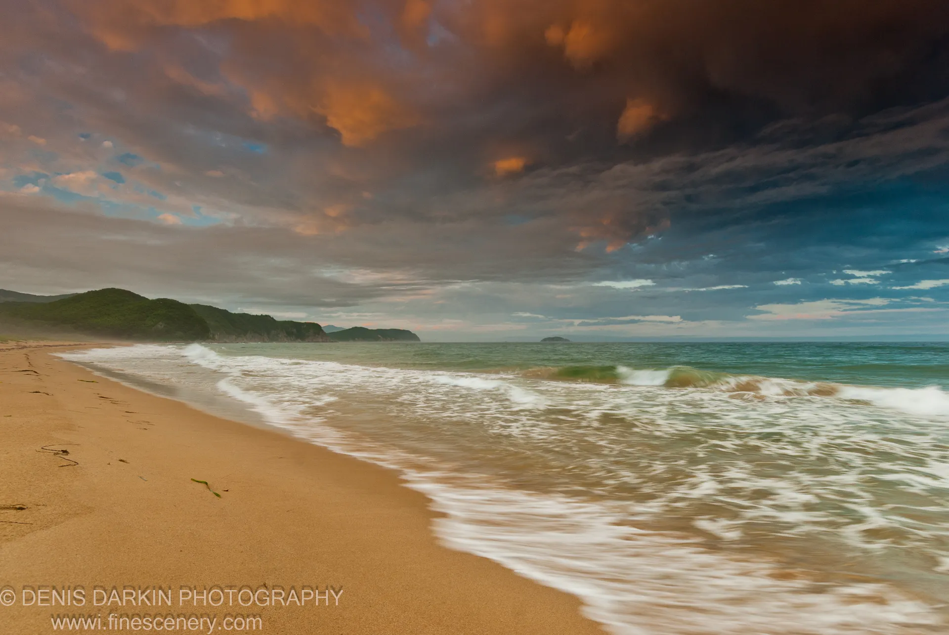 Amber clouds over mist-covered forested headlands at Tachingouza Bay, with warm orange light on the cloud base and the open sea visible below, July 2010.