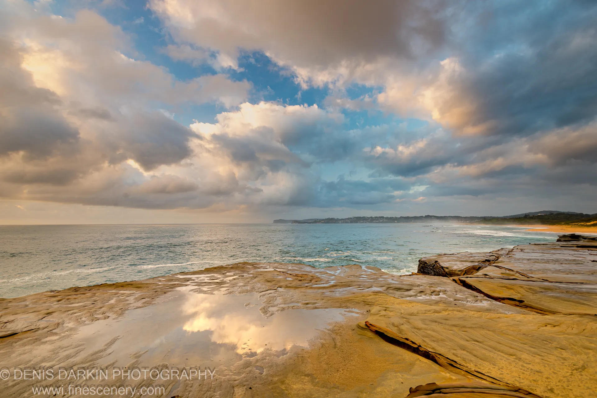 Wet sandstone rock planes at Spoon Bay mirror the cloud formations above at dawn, with warm light on the stone edges.