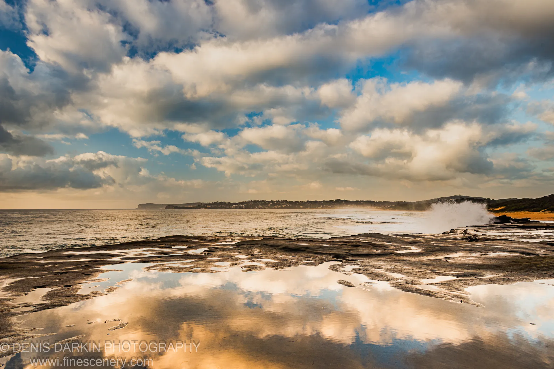 Wet sandstone rock shelf at Spoon Bay reflects cumulus cloud formations in early summer morning light on the Central Coast of New South Wales.