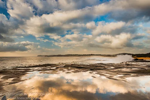 Wet sandstone rock shelf at Spoon Bay reflects cumulus cloud formations in early summer morning light on the Central Coast of New South Wales.