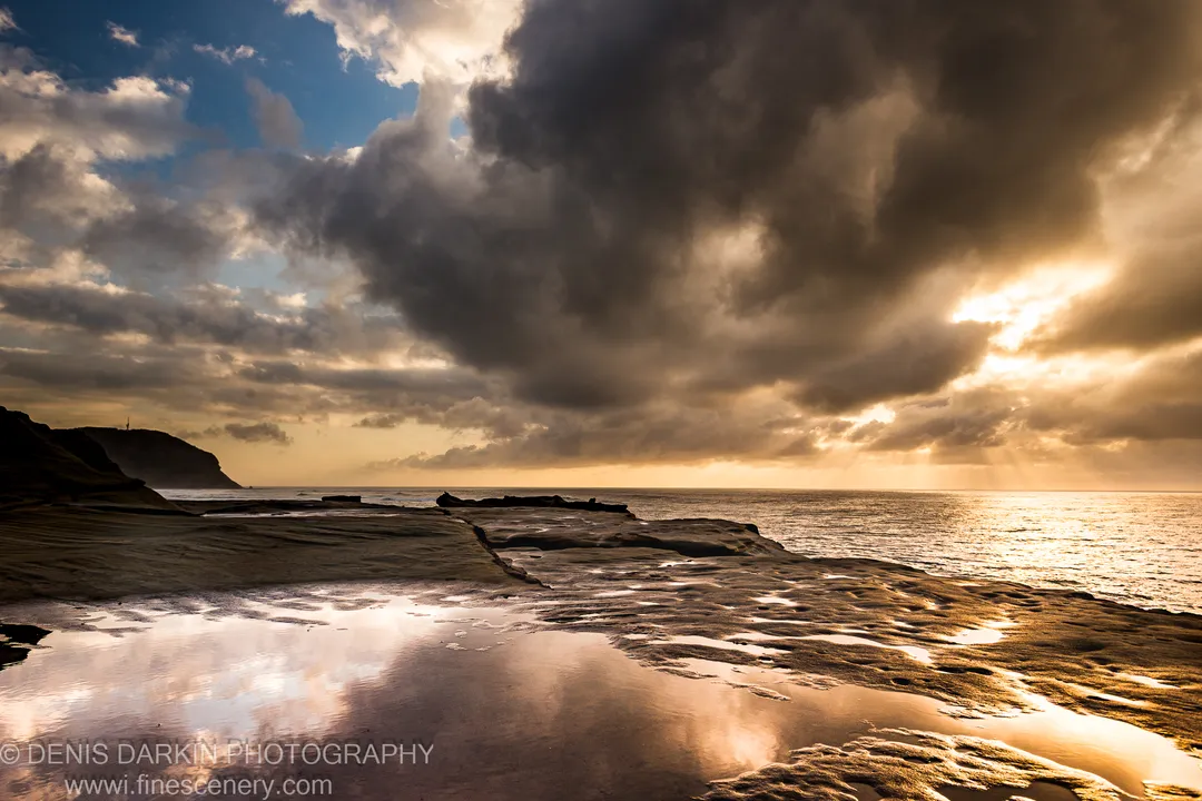 Storm clouds over a coastal tidal pool at Spoon Bay as morning light breaks through the dark cover above the ocean.