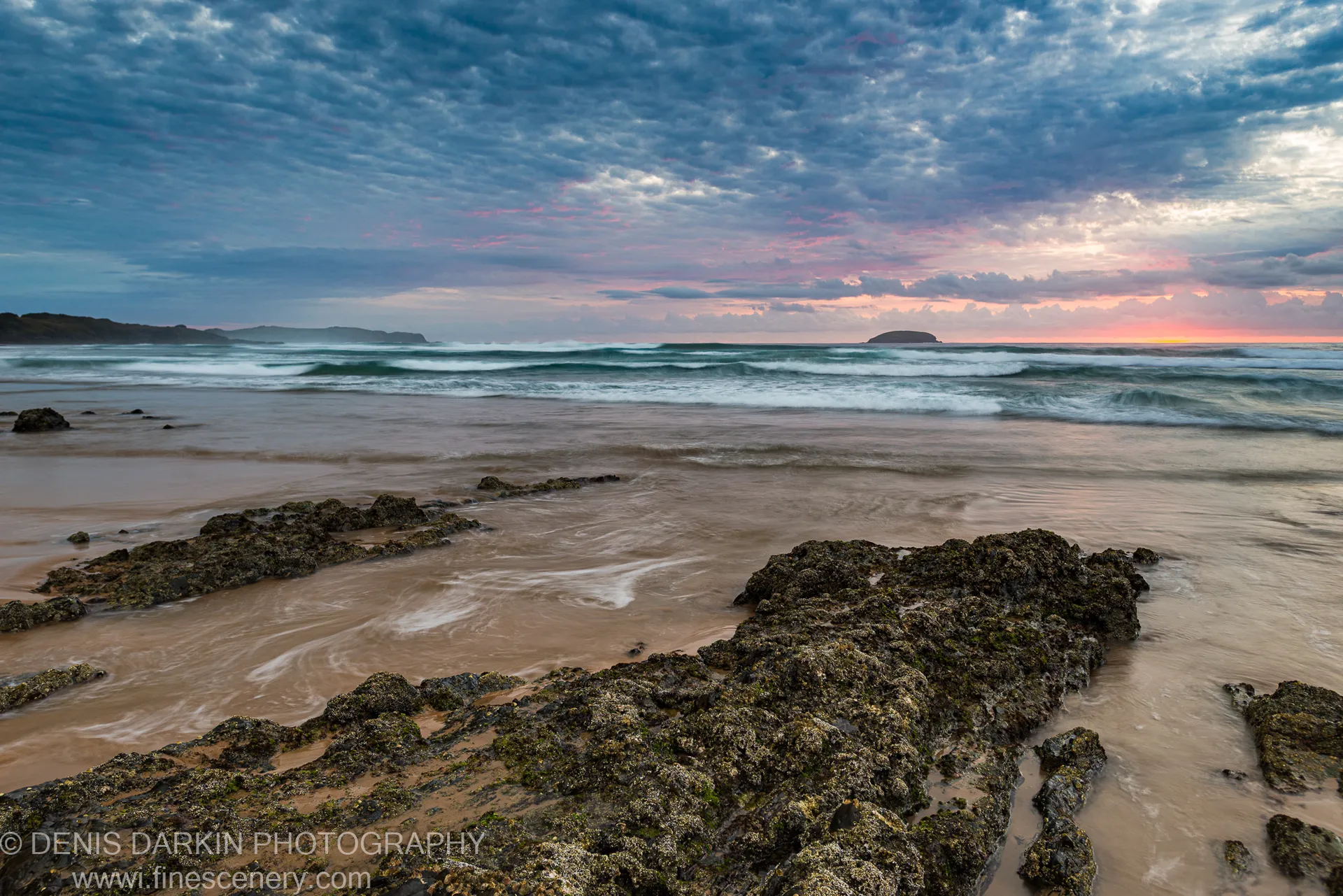Algae-covered rocks in the foreground, with long-exposure waves and a bright horizon under blue cloud cover, Gold Coast, Queensland.