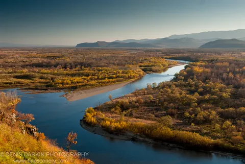 From a rocky cliff edge in Primorsky Krai, the Iman River meanders below through golden autumn forest toward hazy mountain ranges.