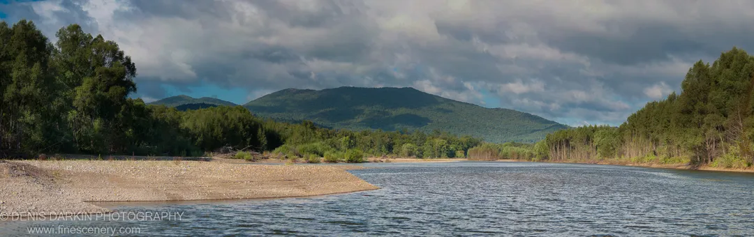 A wide gravel spit on the Bikin River leads toward dense forested mountain ridges under heavy cloud and blue patches, September 2010.