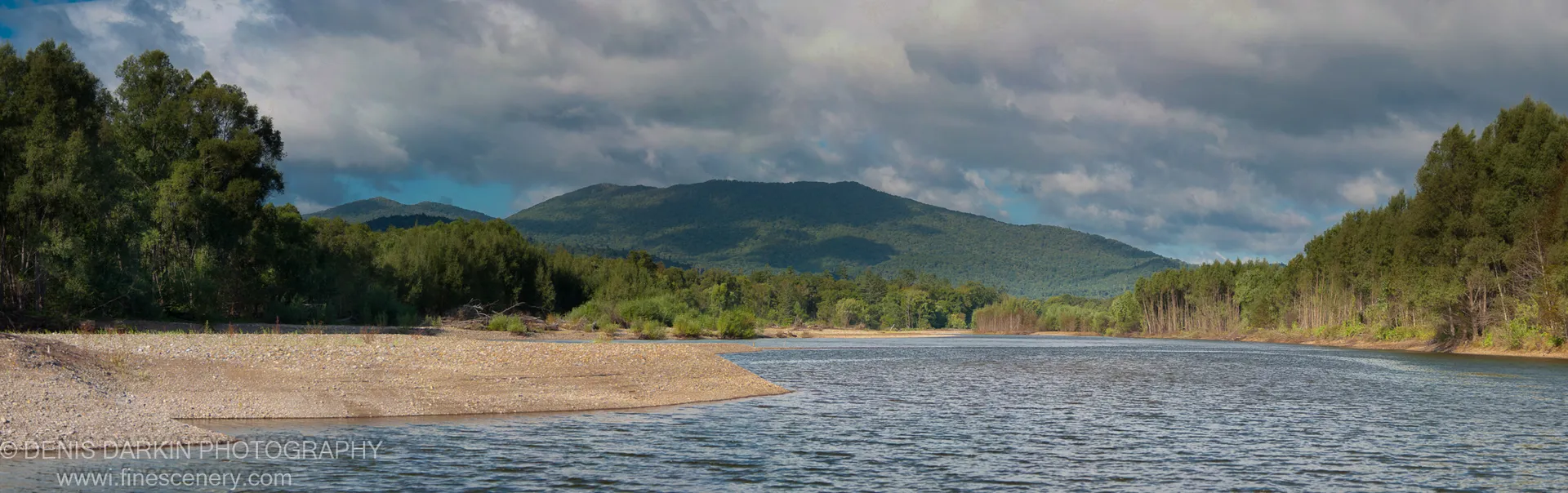 A wide gravel spit on the Bikin River leads toward dense forested mountain ridges under heavy cloud and blue patches, September 2010.