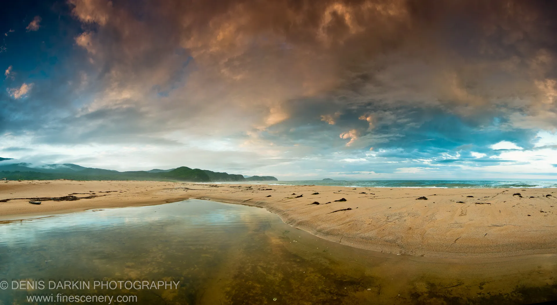 Warm sunset clouds over dark coastal hills and the ocean at Tachingouza Bay, with wet sand and shallow water in the foreground, July 2010.