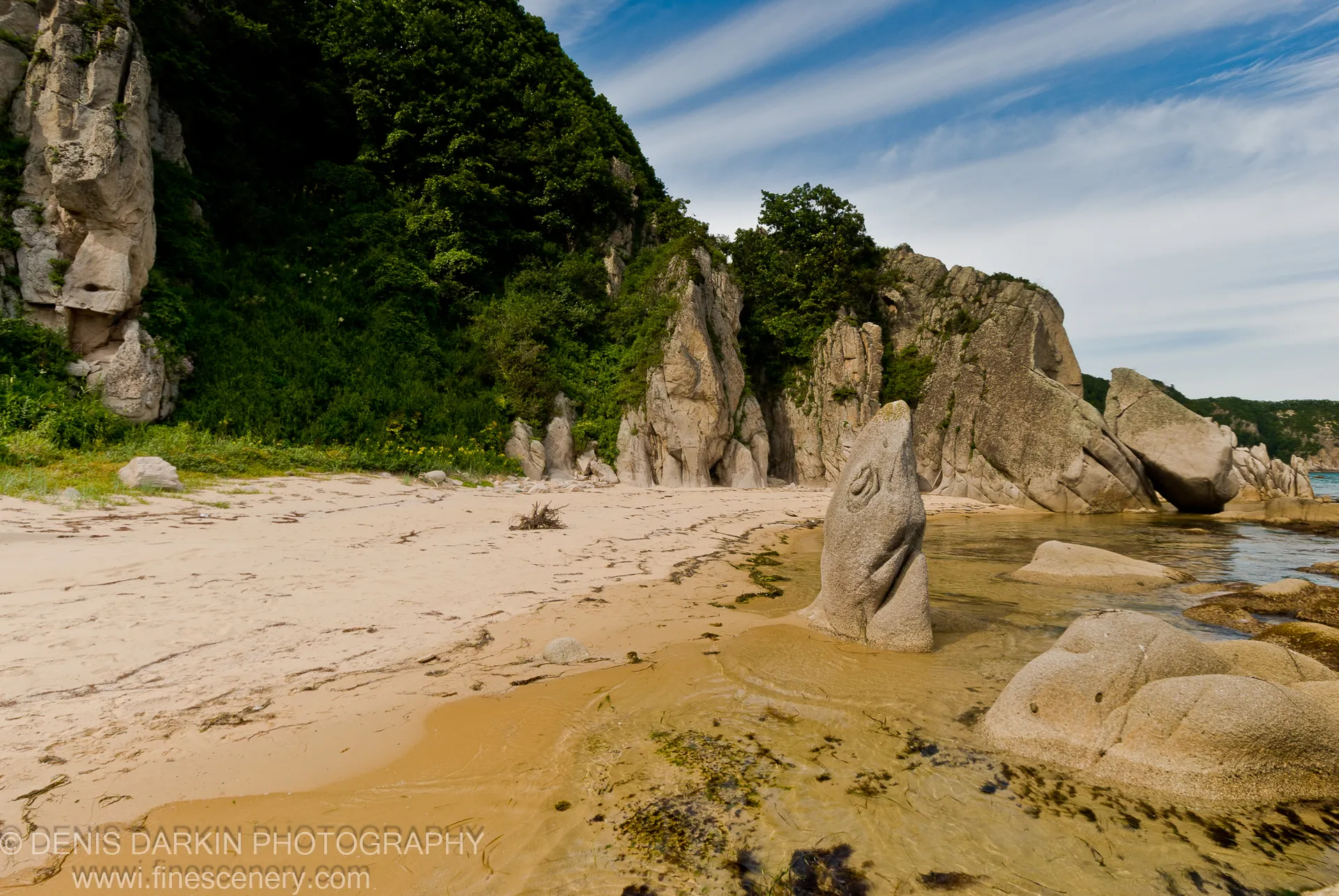 Massive granite boulders rise from clear shallow water in a secluded cove at Lazovsky Reserve, below a steep forested cliff.