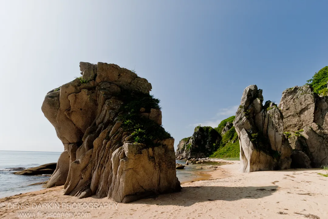 Two granite formations rise from the sandy beach at Tachingouza Bay, Lazovsky Reserve, with a sheltered cove visible between them.