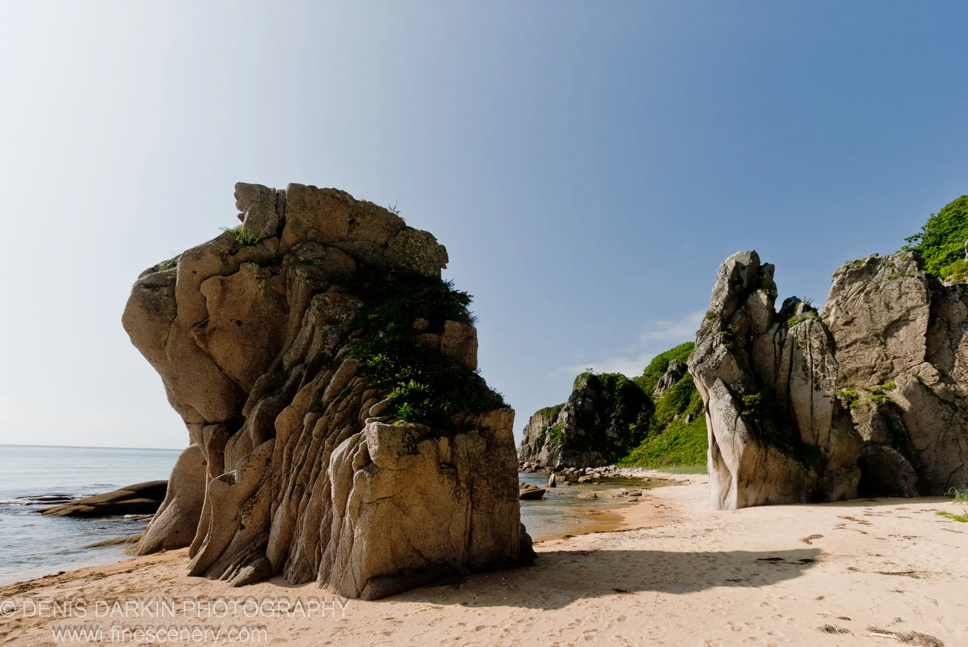 Two granite formations rise from the sandy beach at Tachingouza Bay, Lazovsky Reserve, with a sheltered cove visible between them.