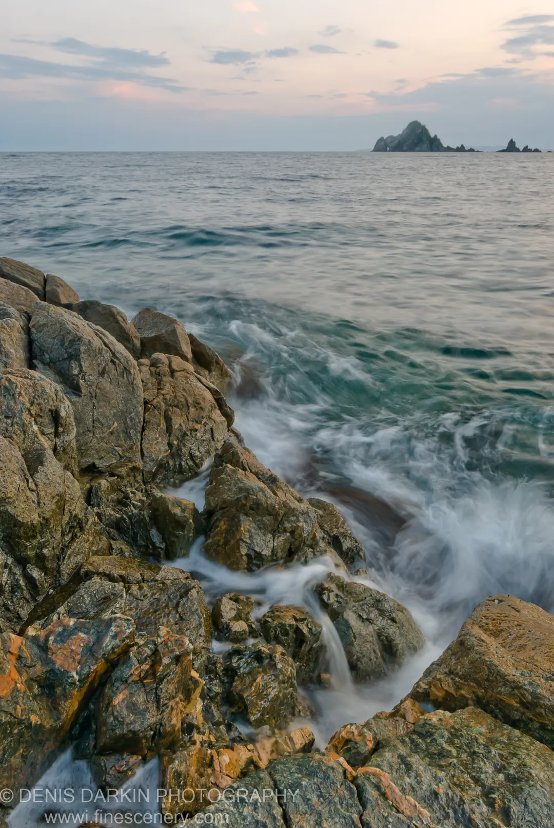 Long-exposure view of wet grey stones and white water at Vityaz Bay, with dark sea stacks against the evening sky.
