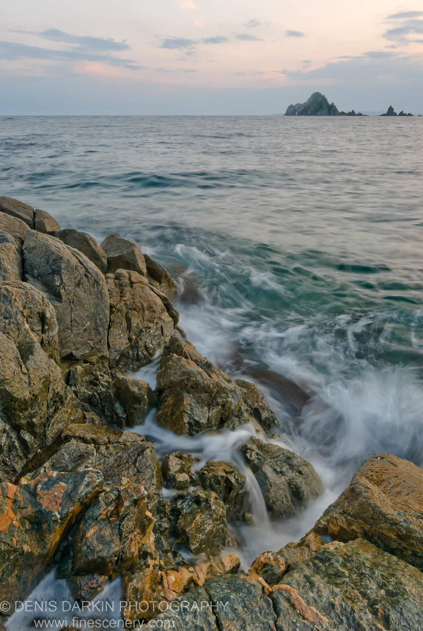 Long-exposure view of wet grey stones and white water at Vityaz Bay, with dark sea stacks against the evening sky.