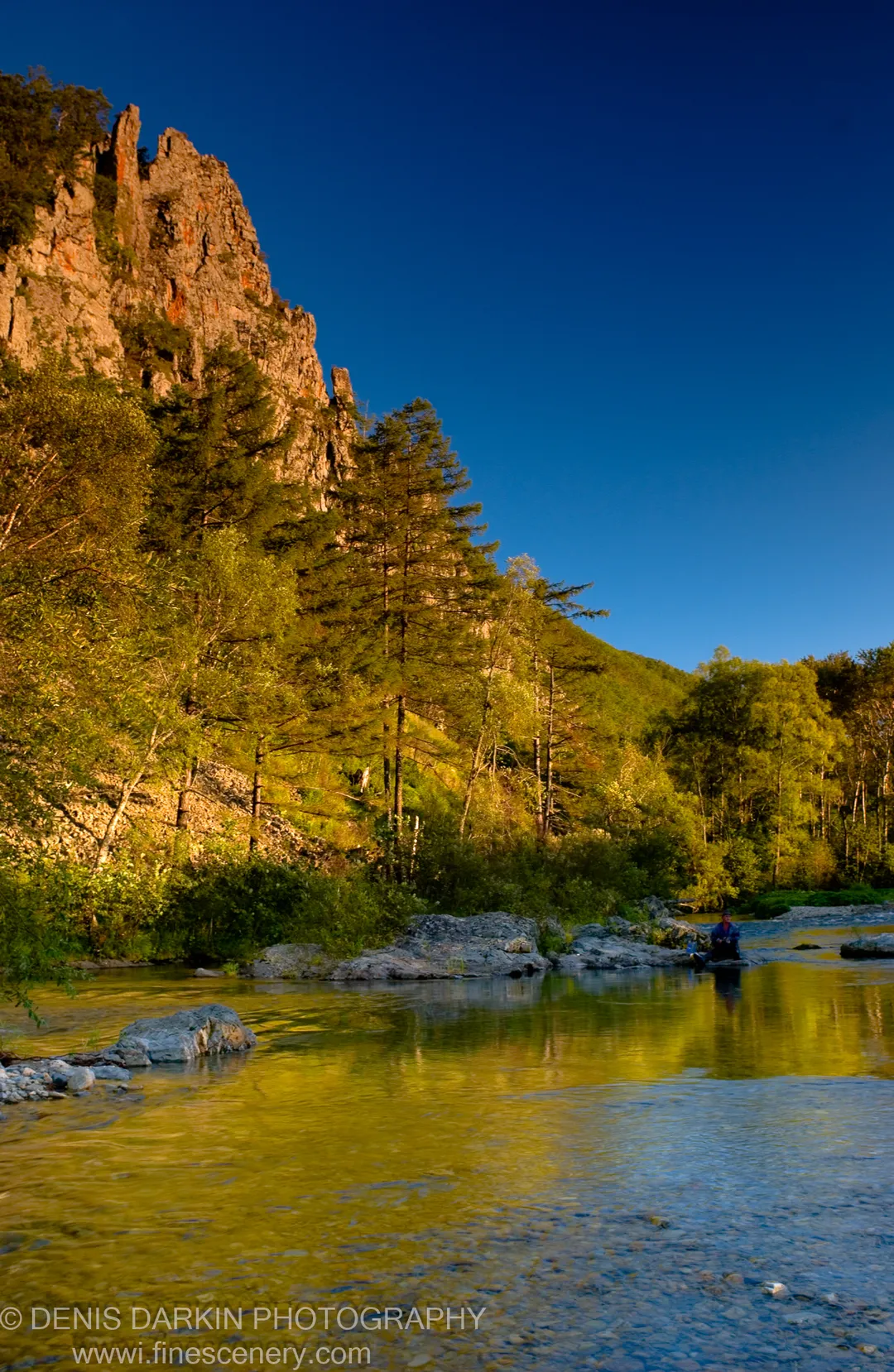 Warm sunlight on a steep rocky cliffside above a clear shallow river, deep blue sky overhead, Plastun, Primorsky Krai, September 2006.