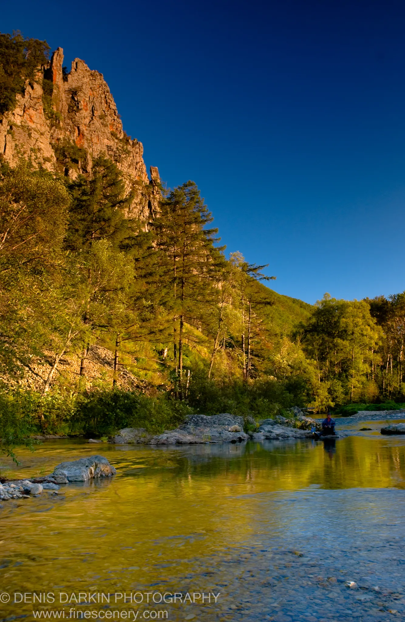 Warm sunlight on a steep rocky cliffside above a clear shallow river, deep blue sky overhead, Plastun, Primorsky Krai, September 2006.