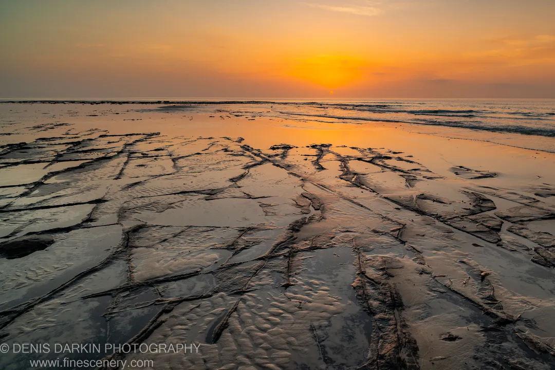 Low-tide rock platform at Huskisson with dark fissures and shallow water channels lit by early dawn light, New South Wales coast.