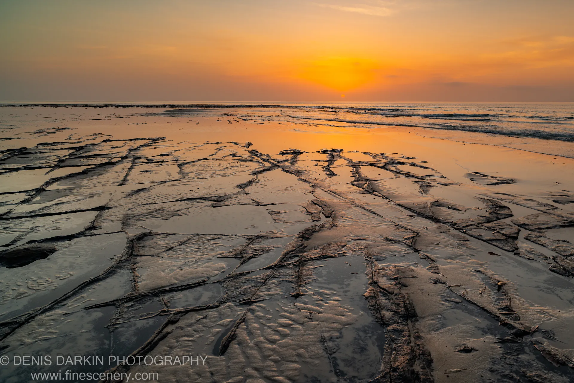 Low-tide rock platform at Huskisson with dark fissures and shallow water channels lit by early dawn light, New South Wales coast.