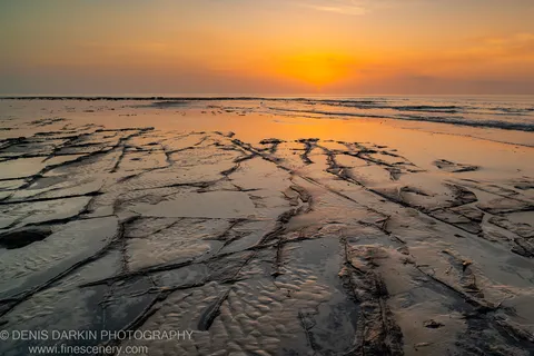 Low-tide rock platform at Huskisson with dark fissures and shallow water channels lit by early dawn light, New South Wales coast.