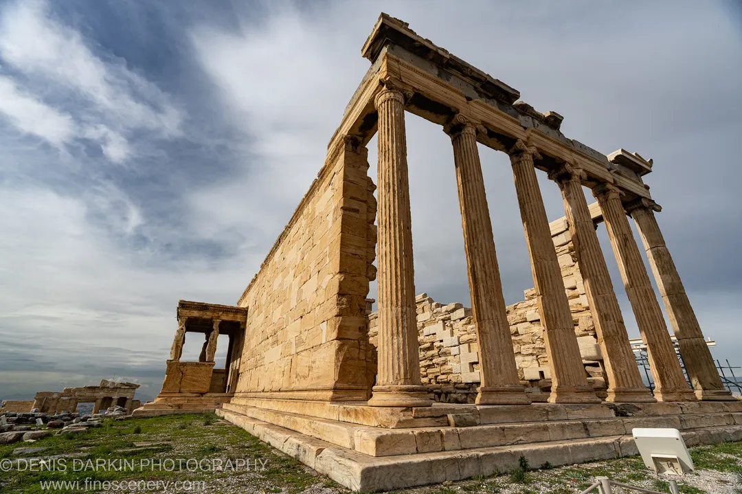 Tall fluted columns of ancient marble stand against a clouded winter sky above the ruins of Athens.