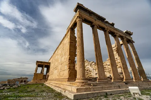Tall fluted columns of ancient marble stand against a clouded winter sky above the ruins of Athens.
