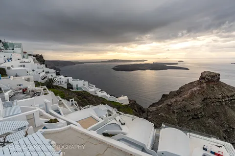White-washed terraced buildings descend the volcanic cliffs overlooking the dark caldera sea, Santorini, December 2024.