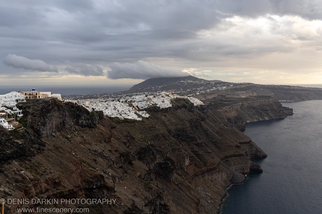 Heavy clouds hang over barren volcanic slopes and the distant caldera sea, Santorini, December 2024.