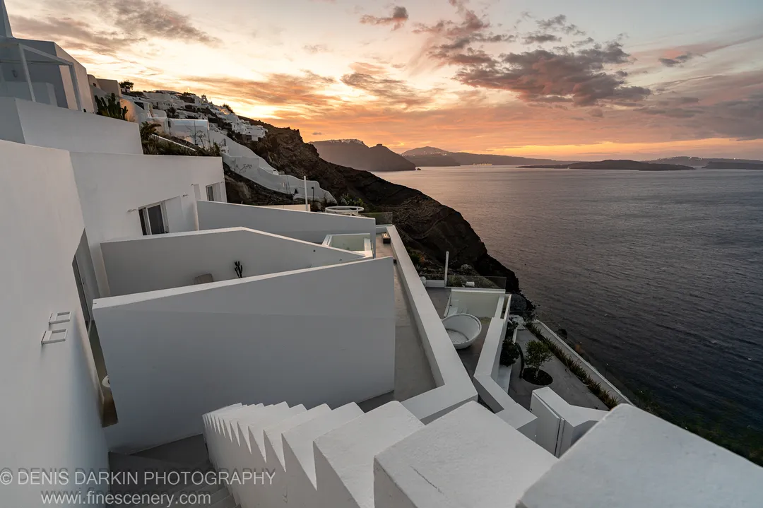 White-washed plaster walls on a Santorini cliffside catching cool blue pre-dawn light, with warm tones at the horizon as sunrise approaches, December 2024.