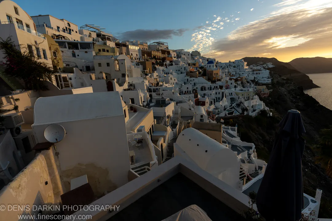 Wide-angle view of white cubic buildings stepping down the volcanic caldera rim at dawn in Santorini, December 2024.
