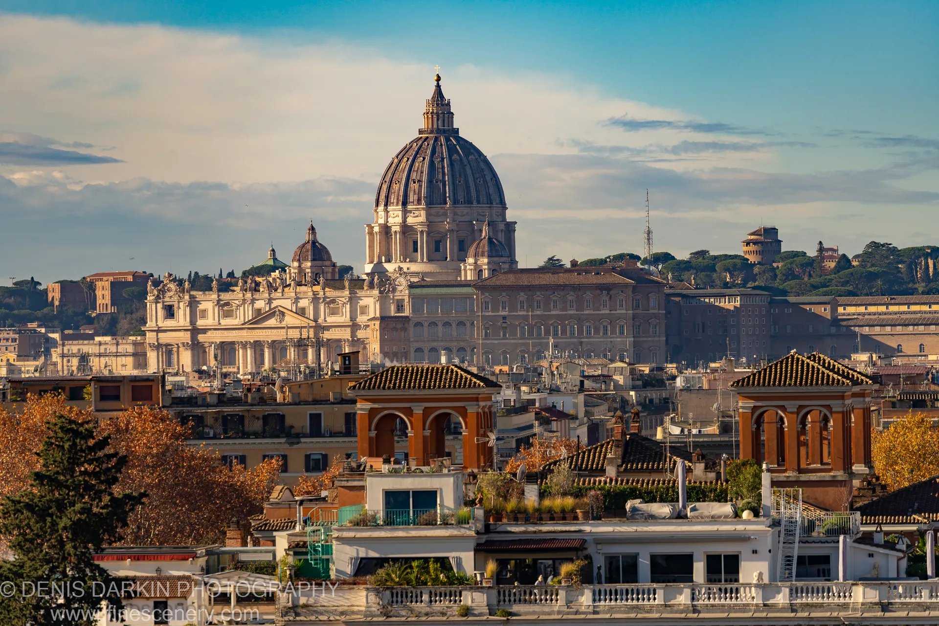 A domed basilica in Rome seen above terracotta rooftops in winter morning light, stone facade catching low sun against a clear sky.