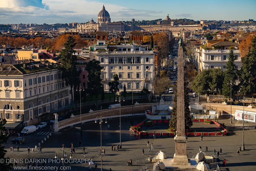 View over Piazza del Popolo in Rome, with the Egyptian obelisk and a Christmas tree below, St. Peter's dome on the winter horizon.