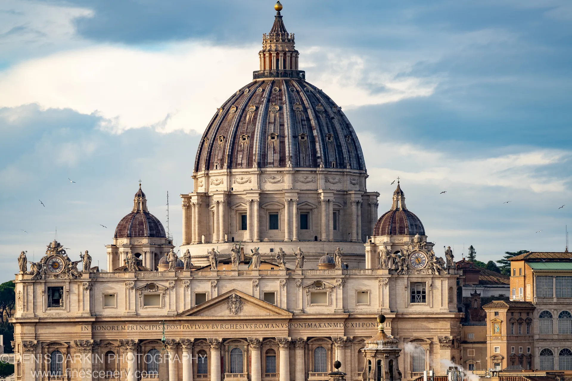 St. Peter's Basilica dome from below in Rome, oxidized copper ribs and stone statues against a winter morning sky.