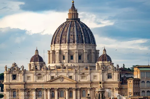 St. Peter's Basilica dome from below in Rome, oxidized copper ribs and stone statues against a winter morning sky.