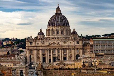 Large dome and stone statues above the terracotta rooftops of Rome, soft midday cloud diffusing winter light across the cityscape.