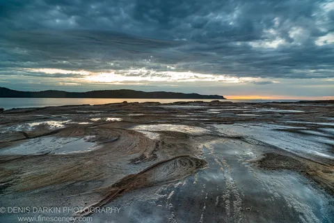 Striated sedimentary rock platforms at Umina Beach stretch to the horizon before sunrise, tide pools reflecting a blue-grey predawn sky.