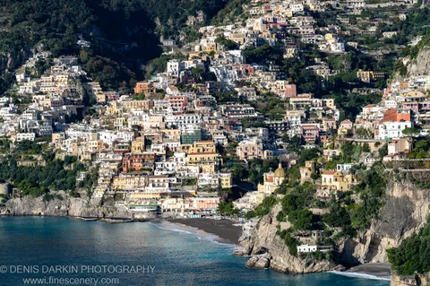 Pastel buildings on a steep cliffside above a black-sand beach at Sorrento, with a golden church dome visible among the tightly packed terraces.