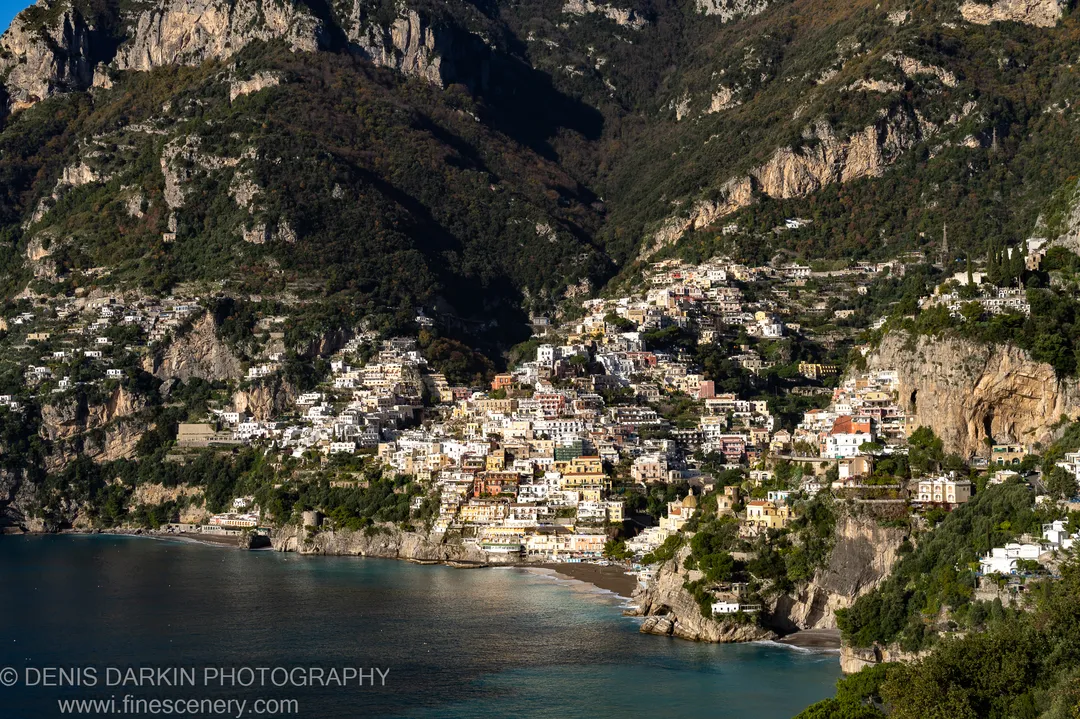 Dense hillside village with warm ochre facades in strong winter sunlight on the steep slope above the blue bay at Sorrento.