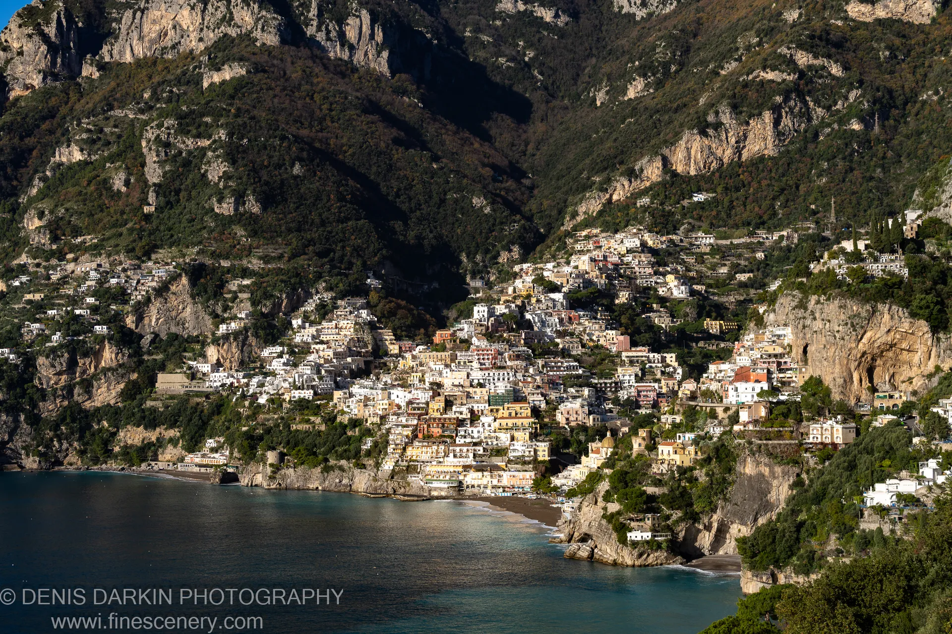 Dense hillside village with warm ochre facades in strong winter sunlight on the steep slope above the blue bay at Sorrento.