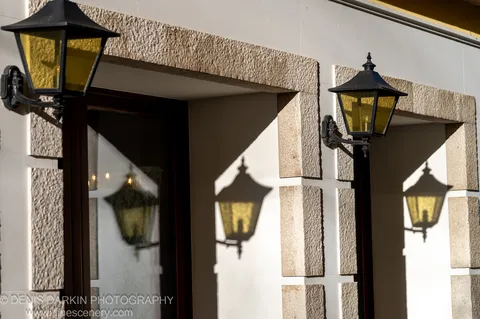 Two black lanterns flank stone blocks on a Venetian wall, their shadows cast sharply on white plaster in winter sun.