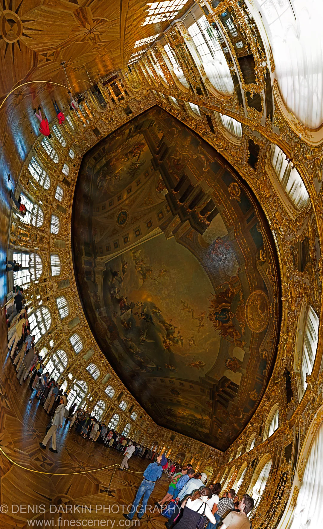 Fisheye view inside a grand palace hall in St Petersburg, with a frescoed ceiling and ornate mirrored walls encircling visitors below.
