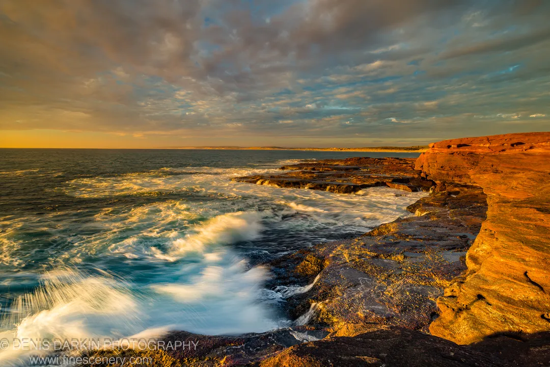 Stratified red rock formations line the reef platform at Red Bluff as long-exposure waves smooth to pale white across the foreground.