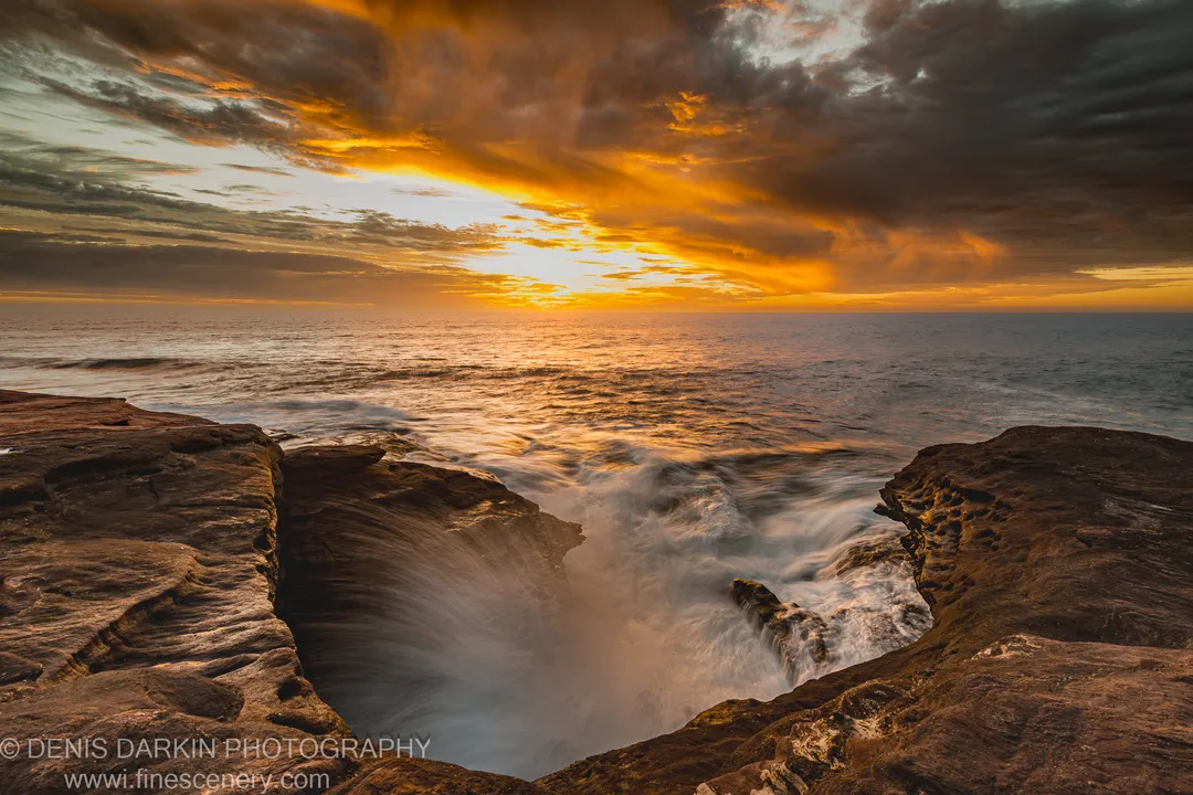 A natural pool in the sandstone platform at Red Bluff collects blurred wave water as storm clouds part to reveal evening light.